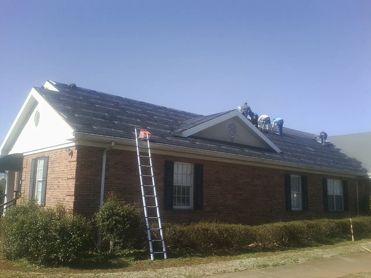 Crew tearing shingles off a brick ranch roof with a ladder set — Emergency Roof Repair work by our crew in Orland