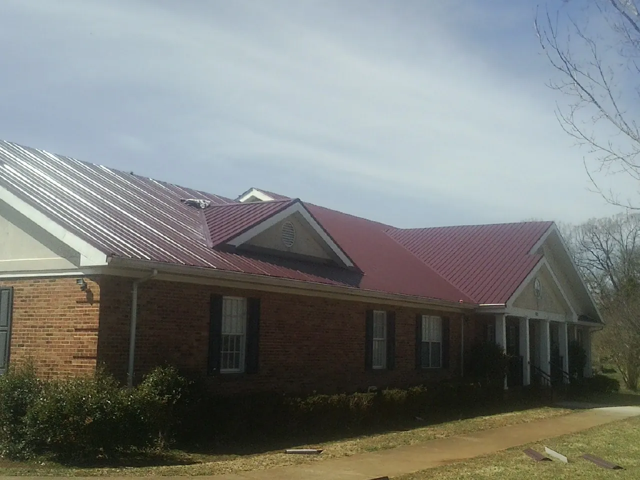 Red metal roof with gabled entries on a long brick building, from a Hail Damage Roof Repair job in Orland