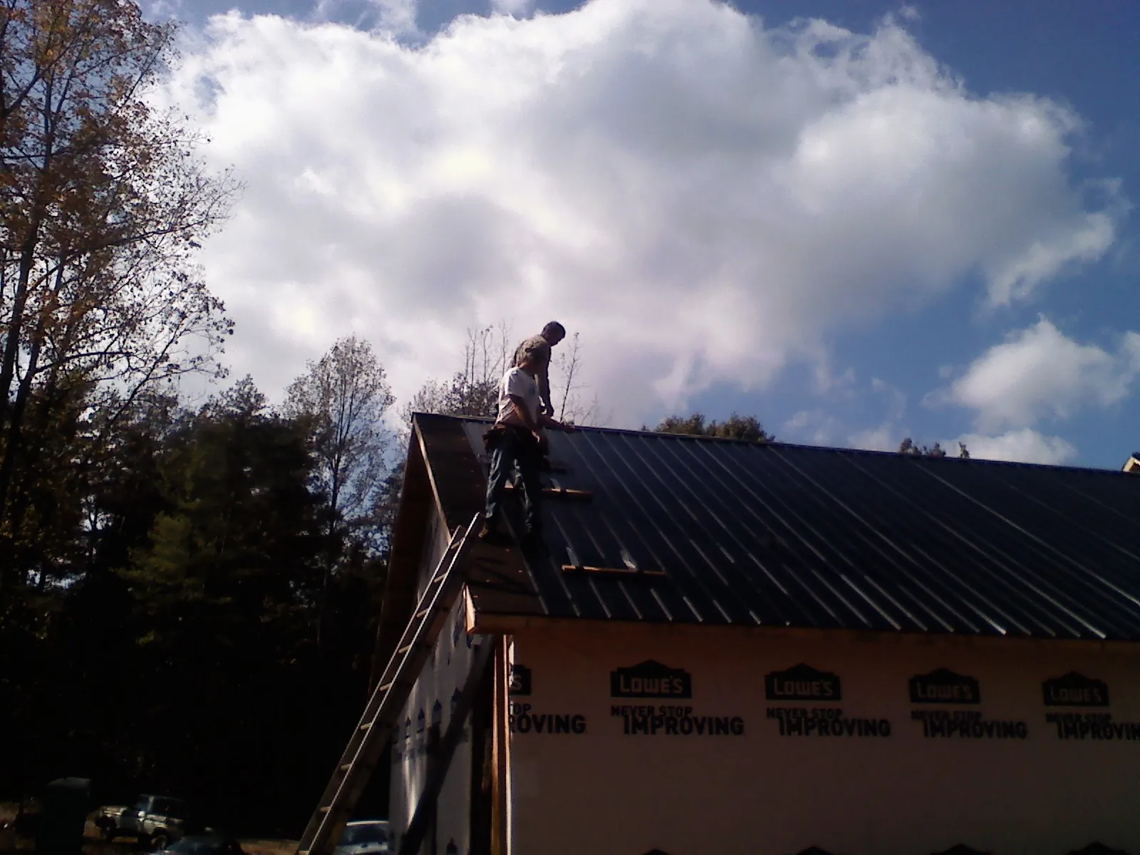 Roofer fastening dark metal panels high against a cloudy sky, from a Roof Inspection job in Orland